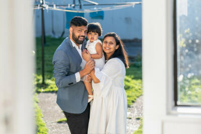 A man, woman, and toddler at home, smiling at the camera.