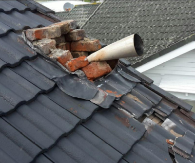 A chimney collapsed on a roof, with bricks and tiles broken around it.