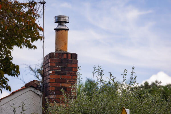 A brick chimney on top of a home that has been partially removed and replaced by a metal flue.