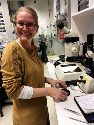 A woman standing in front of a microscope smiling.