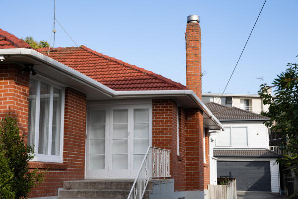 The outside of a New Zealand home, with red brick walls and a tall brick chimney.