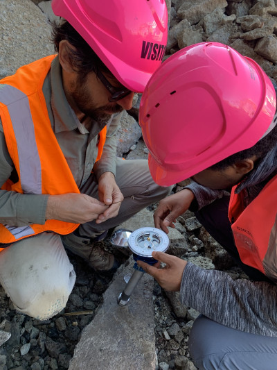 Two researchers in hard hats measure volcanic activity on a rocky mountain,