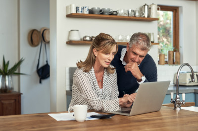 Two people sit at their kitchen bench looking at a laptop