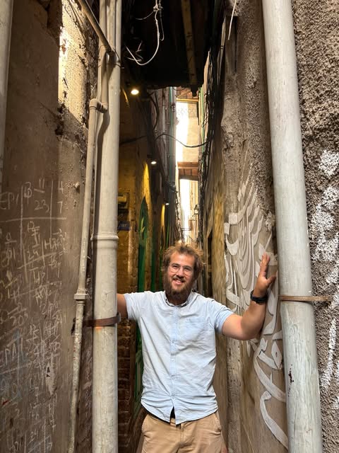 Photo of Joel Bishop standing between two buildings, smiling.
