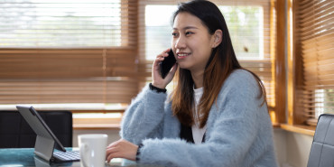 Woman sits at dining room table with her laptop open talking on the phone