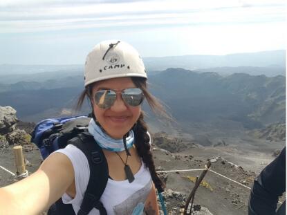 A woman standing at the top of a volcano taking a selfie.