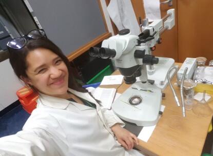 A woman sitting in a lab coat infront of a microscope.
