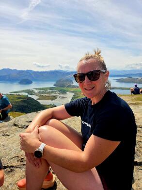 Woman sitting on top of a mountain smiling at the camera.