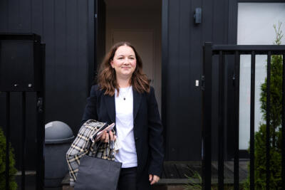 A young woman dressed in business clothes, standing in front of her front door.