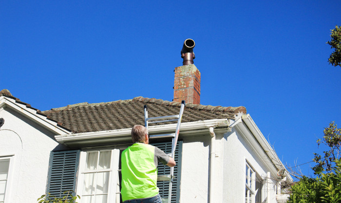 Builder climbs ladder to check the chimney on a roof