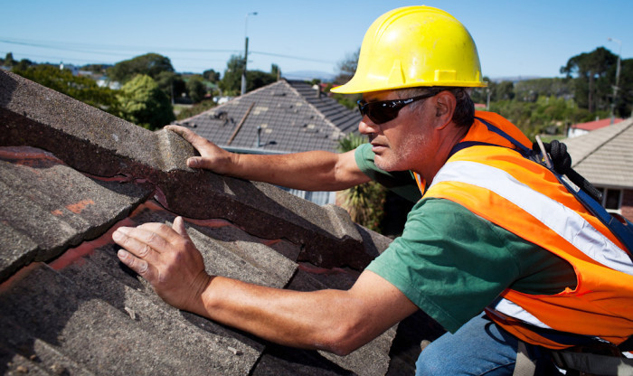 A builder on the roof of a house checks the tiles are secure